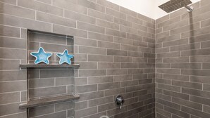 A shower area with grey tiles, a showerhead, and two blue star-shaped decorations on shelves.