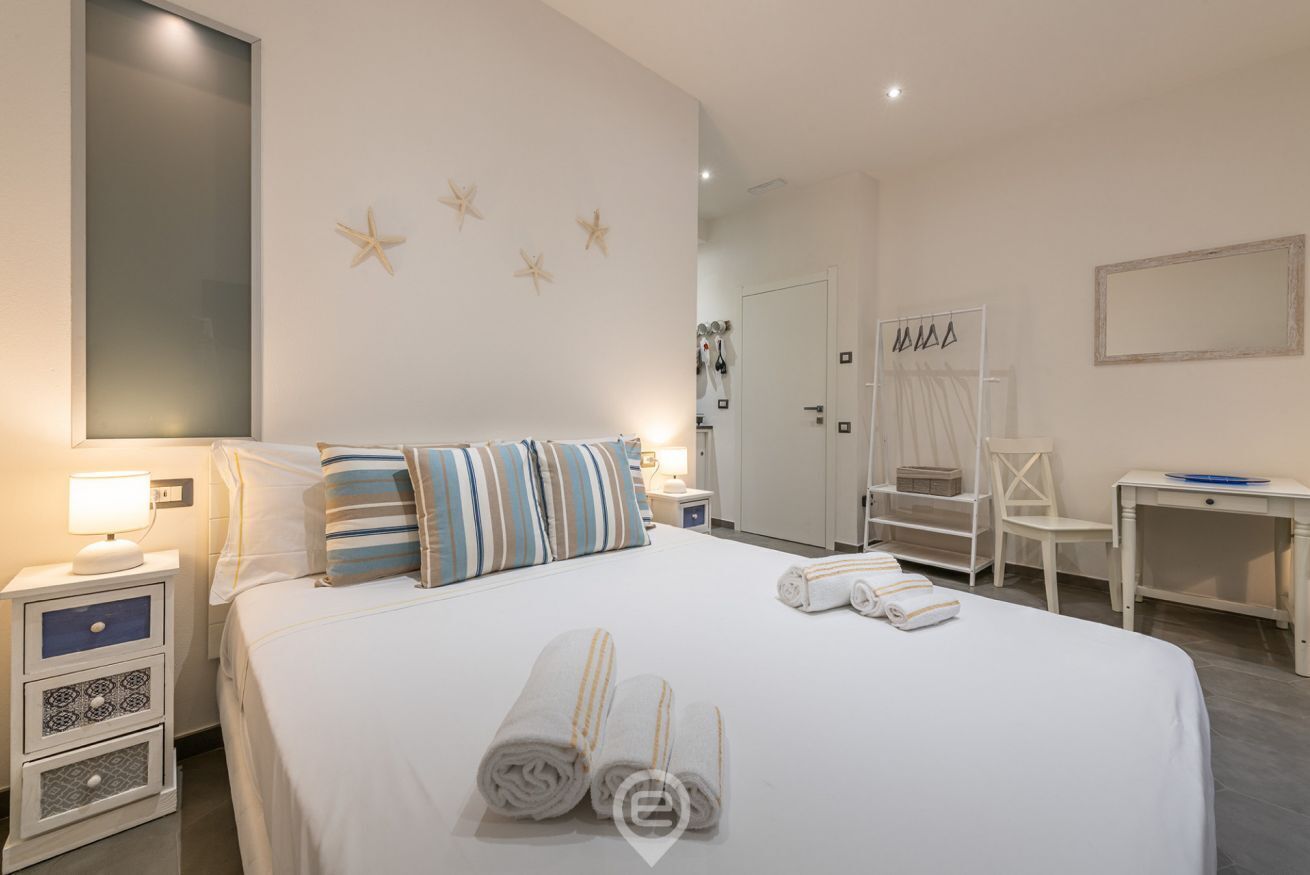 A hotel room with a large bed, a desk, and a chair. There are starfish on the wall and towels on the bed.
