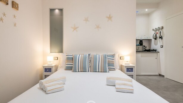 A hotel room with a large bed, two bedside tables with lamps, starfish wall decor, and a view of the kitchen area.