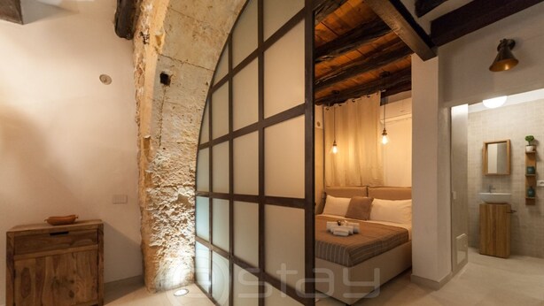 A bedroom with a bed, a wooden cabinet, and a stone wall.