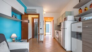 Eine kompakte Küche mit weißen Geräten, einer blauen Akzentwand und einer kleinen Essecke mit Tisch und Stuhl.