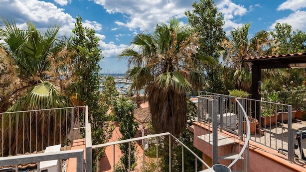 Eine Terrasse mit Blick auf einen Yachthafen, umgeben von Palmen und Kübelpflanzen.