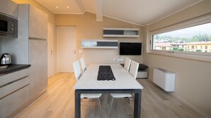 Een moderne keuken met een eettafel, witte stoelen, een flatscreen-tv en een groot raam met uitzicht op gebouwen.