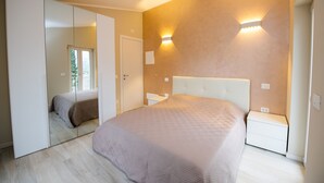Een slaapkamer met een groot bed, een kledingkast, een nachtkastje en een wandlamp.