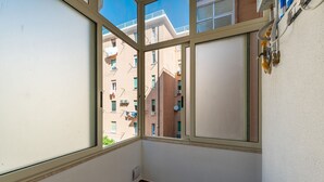 En balkong med utsikt över de omkringliggande byggnaderna, ett fönster med utsikt och en väggmonterad luftkonditioneringsanläggning.