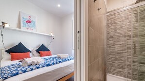 Ett hotellrum med en säng, en dusch och en vägghylla med en tavla som föreställer en flamingo.