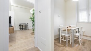 Una habitació moderna i ben il·luminada amb zona de menjador que inclou una taula, cadires, una taula auxiliar i una planta en test.