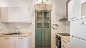 Eine kleine Küche mit weißen Schränken, einem grünen Schrank mit Glastüren, einer Spüle, einem Backofen und einer Arbeitsplatte.
