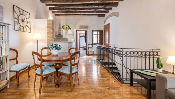 Ein Essbereich mit Holzkästen und einem Tisch, eine Treppe mit schmiedeeisernem Geländer sowie eine Küche im Hintergrund.