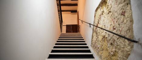 A staircase with a black railing leading to a room with exposed wooden beams and a white wall.