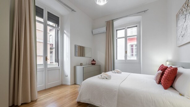 Ein Schlafzimmer mit einem großen Bett, einem Nachttisch, einem Spiegel und einem Fenster mit Vorhängen.
