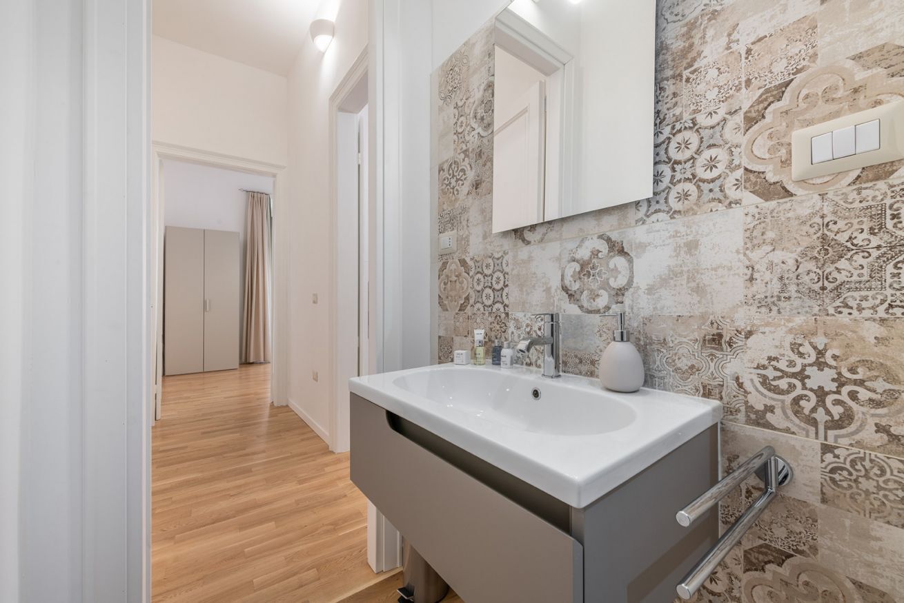 A modern bathroom with a white sink, a mirror, and patterned tiles.
