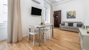 Ein modernes Wohnzimmer mit Essbereich, einem Flachbildfernseher an der Wand, einer Couch mit Kissen und einem Gemälde.