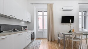 Eine moderne Küche mit weißen Schränken, ein Essbereich mit Tisch und Stühlen sowie ein großes Fenster mit Vorhängen.