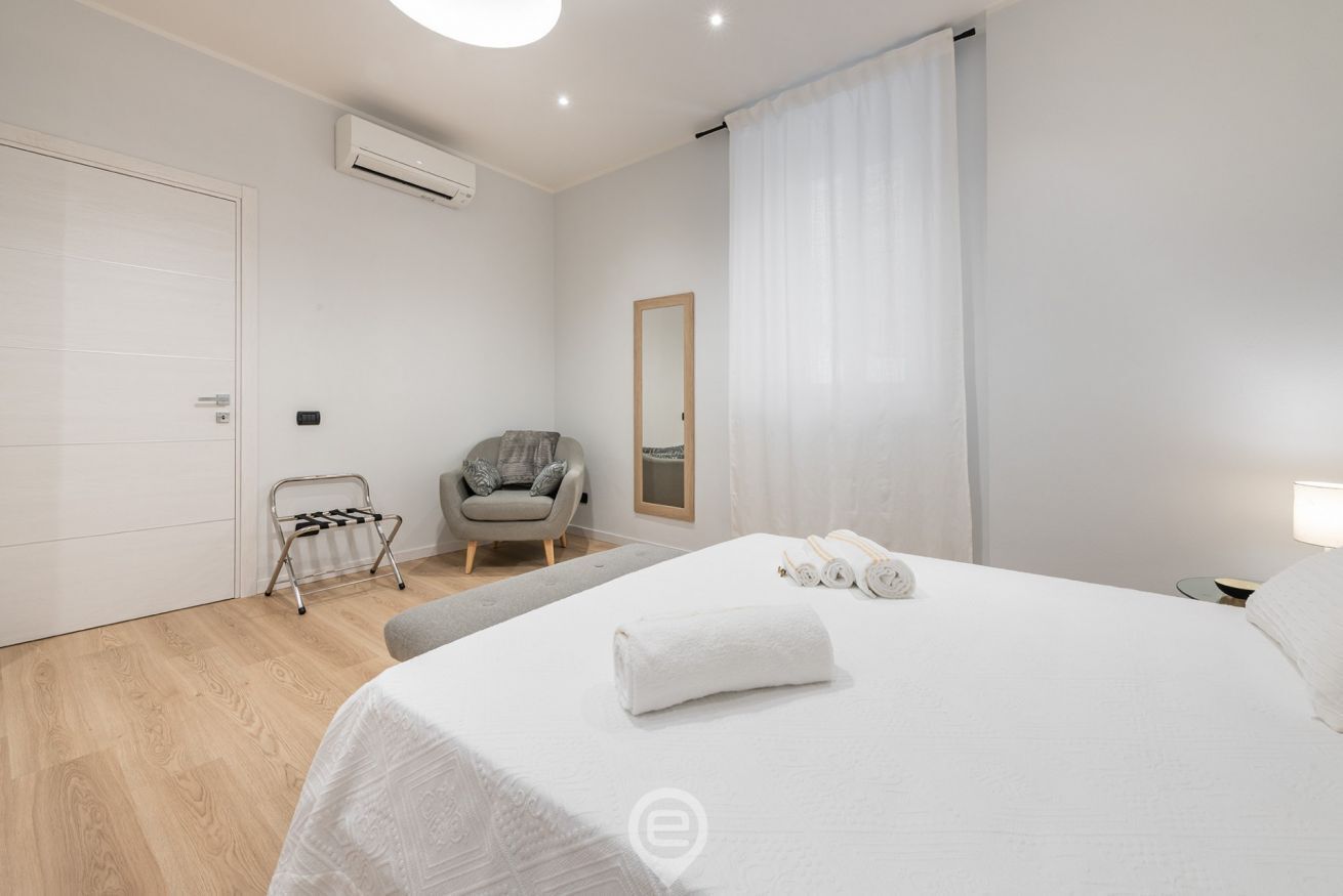 A modern hotel room with a large bed, a chair, a small table, and a mirror.