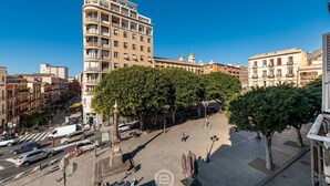 A multi-story building with balconies, a pedestrian area with trees, and a clear blue sky. - Piazza Yenne Apartment (Cagliari)