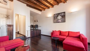 A spacious living area with a red sofa, a red armchair, and a small round table. There is a wooden ceiling and a painting on the wall. - Piazza Yenne Apartment (Cagliari)