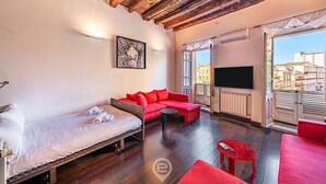 A room with a bed, a red sofa, a red armchair, a small table, and a TV. - Piazza Yenne Apartment (Cagliari)