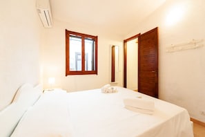 A hotel room with a bed, a window, a door, and an air conditioning unit.
