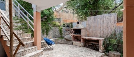 Una escalera de piedra conduce a un patio cubierto con una parrilla, una silla azul y una valla de madera.