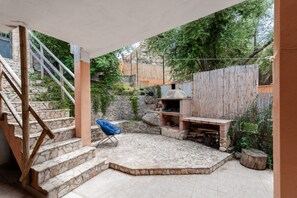 Una escalera de piedra conduce a un patio cubierto con una parrilla, una silla azul y una valla de madera.
