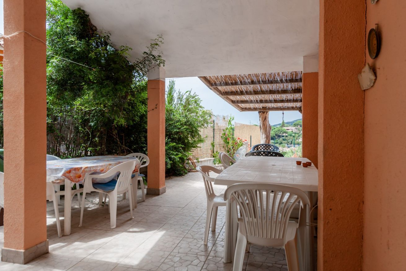 An outdoor patio with a table and chairs, surrounded by greenery and a view of a hill.