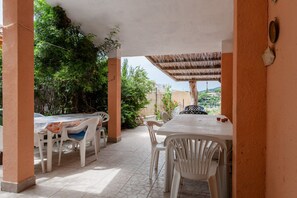 An outdoor patio with a table and chairs, surrounded by greenery and a view of a hill.