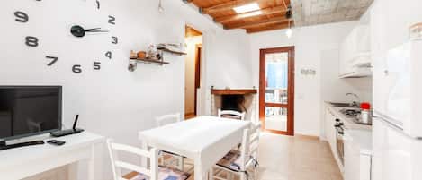 Una cocina con armarios blancos, techo de madera, un reloj en la pared y un televisor sobre una mesa blanca.