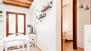 Een kamer met een witte tafel en stoelen, een bed met een witte dekbedovertrek, en een wandplank met decoratieve objecten.