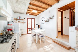 Une cuisine équipée d’une cuisinière à gaz, de meubles blancs et d’un plafond en bois. On y trouve également un coin repas avec une table et des chaises blanches.