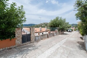 A residential street with houses, a stone wall, and a clear view of the surrounding hills. - Casa Nicole - Near the beach (Quartu Sant'Elena)