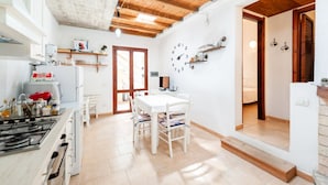 Een keuken met een gasfornuis, witte kasten en een houten plafond. Er is een eethoek met een witte tafel en stoelen.