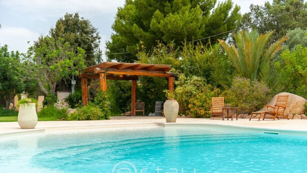A swimming pool with a wooden pergola, lounge chairs, and potted plants.