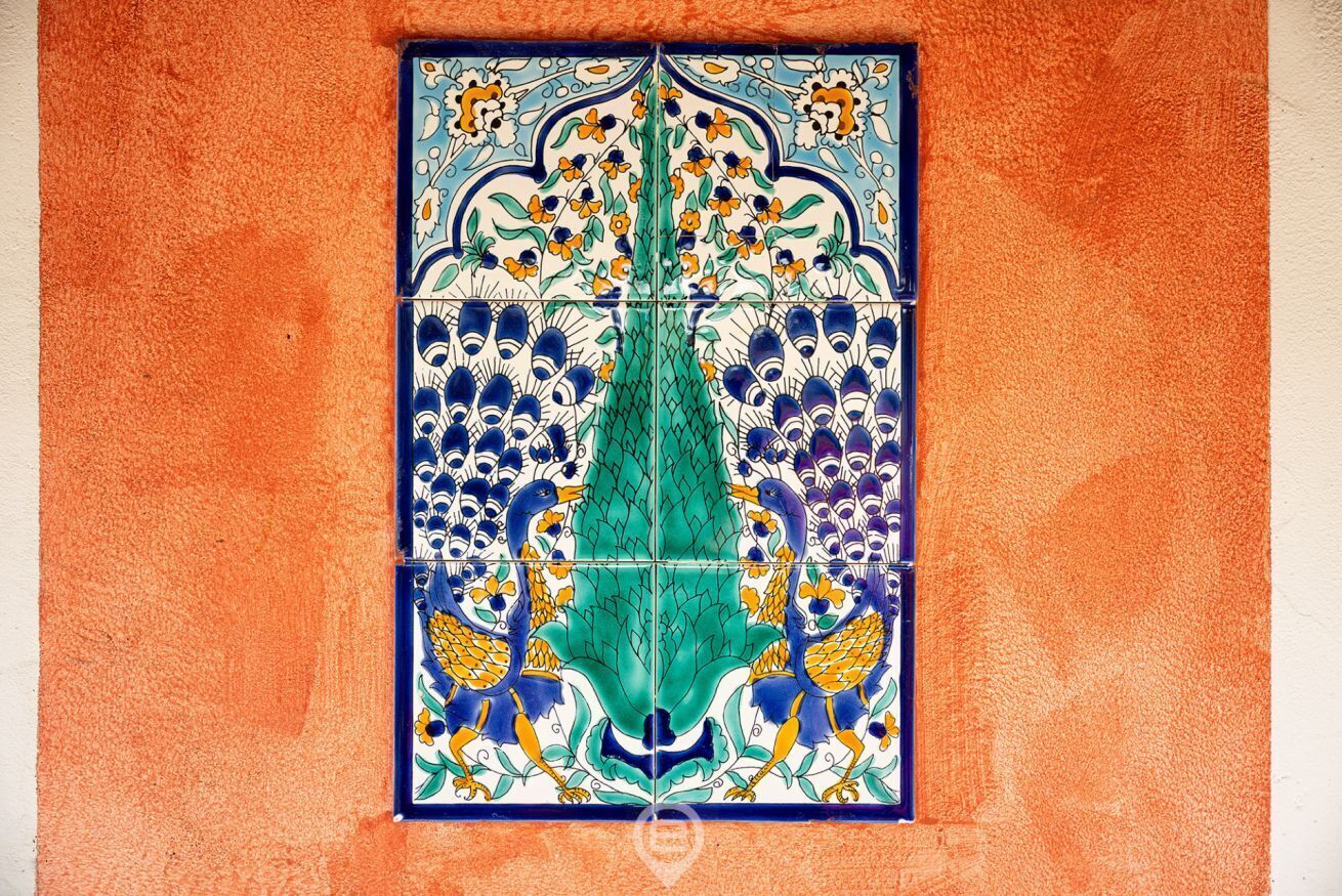 Een decoratieve tegel met een centraal groen bladmotief, omringd door blauwe en gele patronen.
