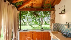A kitchen with a large window, wooden cabinets, a stone wall, and a tiled backsplash.