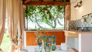 A cozy room with a wooden ceiling, a table set with a vase of greenery, and a window with a view of trees.