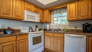 A kitchen with wooden cabinets, a white stove, a dishwasher, and a window with curtains. - Located in the Luxurious Pine Manor Estates! (Carbondale)