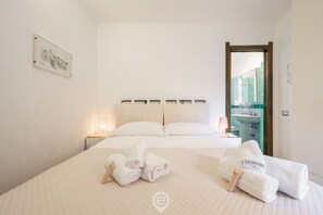Ein ordentlich bezogenes Bett mit weißen Laken und Handtüchern, ein Nachttisch mit Lampe sowie ein gerahmtes Bild an der Wand.