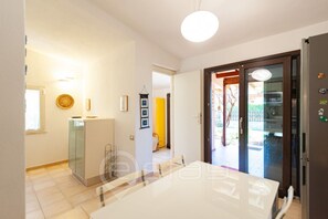 A modern kitchen with a dining area, a refrigerator, and a door leading to a balcony.