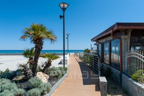 Ein Küstenweg mit einem Restaurant namens "La Cantina del Mar" auf der rechten Seite, Palmen und freiem Blick auf das Meer.