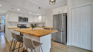 A modern kitchen with white cabinetry, a wooden island, stainless steel appliances, and a pendant light. - Chic Digs Across From Forsyth Park w/ Parking by Lucky Savannah (Savannah)