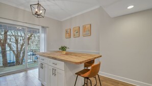 A kitchen with a wooden island, white cabinets, and a bar stool. There are three framed pictures on the wall and a plant on the island. - Chic Digs Across From Forsyth Park w/ Parking by Lucky Savannah (Savannah)