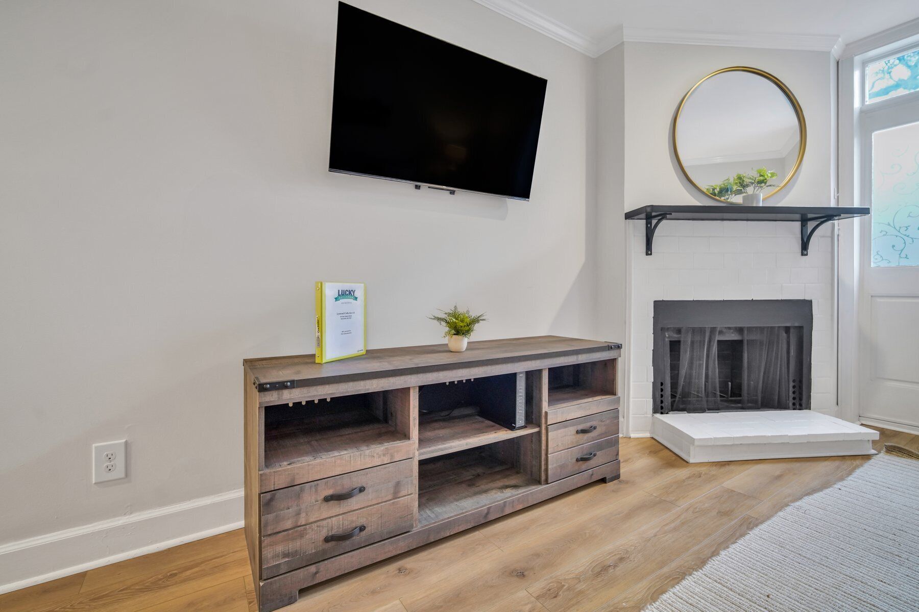 A living room with a flat-screen TV mounted on the wall, a fireplace with a mantel, and a wooden entertainment unit with drawers.