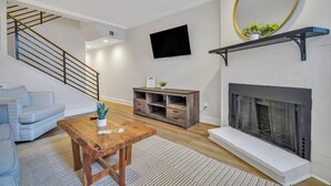 A living room with a staircase, a fireplace, a mounted TV, and a wooden coffee table. - Chic Digs Across From Forsyth Park w/ Parking by Lucky Savannah (Savannah)