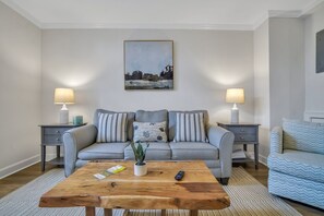 A living room with a grey sofa, two side tables with lamps, a wooden coffee table, and a painting on the wall.