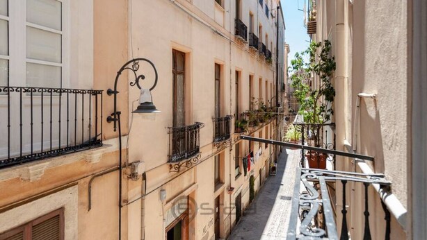 A narrow street with buildings on both sides, featuring balconies with railings and potted plants. - KyS Castello - Suite Lamarmora (Cagliari)