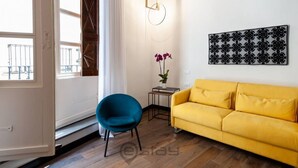 A room with a yellow sofa, a blue chair, a small table with a plant, and a wall-mounted light fixture. - KyS Castello - Suite Lamarmora (Cagliari)