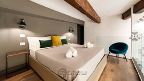 A modern bedroom with a large bed, a nightstand, a chair, and a window with a view. - KyS Castello - Suite Lamarmora (Cagliari)