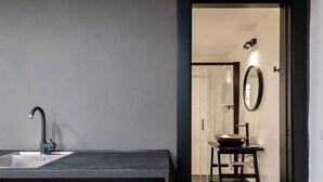 A modern bathroom with a dark countertop, a single sink with a faucet, a mirror, and a small stool with a bowl. - KyS Castello - Suite Lamarmora (Cagliari)