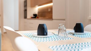 Un coin repas moderne avec une table dressée pour deux personnes, agrémenté d’une carafe à eau en verre transparent et de deux tasses noires posées sur une nappe à motifs.